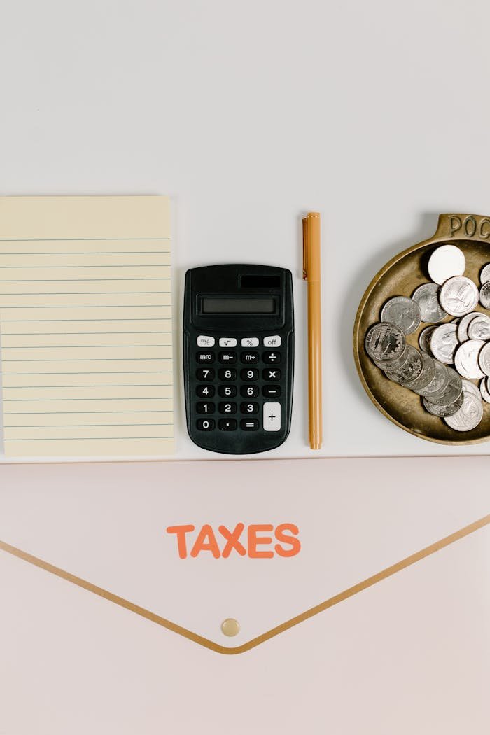 Flat lay of tax preparation tools including a calculator, notebook, and coins.